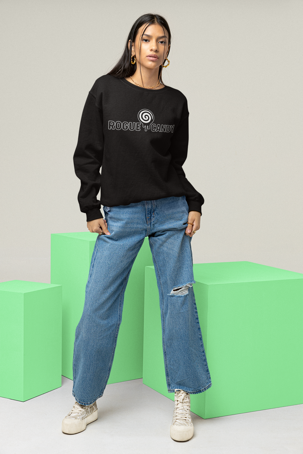 Person wearing a black sweatshirt with a logo and blue jeans on green blocks.