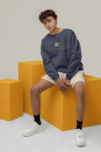 Person wearing a blue sweatshirt with a logo, sitting on orange blocks against a plain background