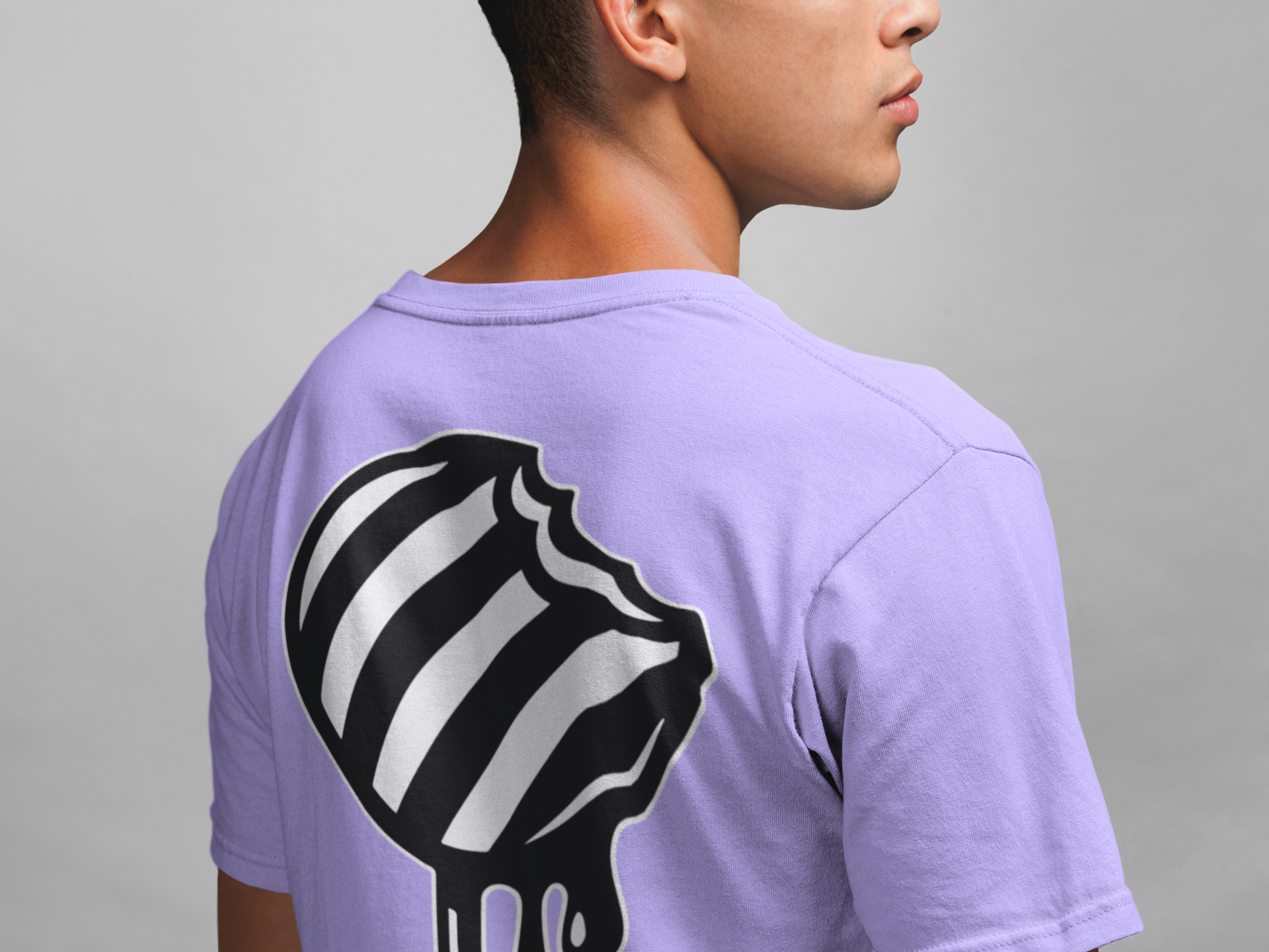 Man wearing a light purple t-shirt with a black and white striped round candy on stick graphic design on the back against a gray background