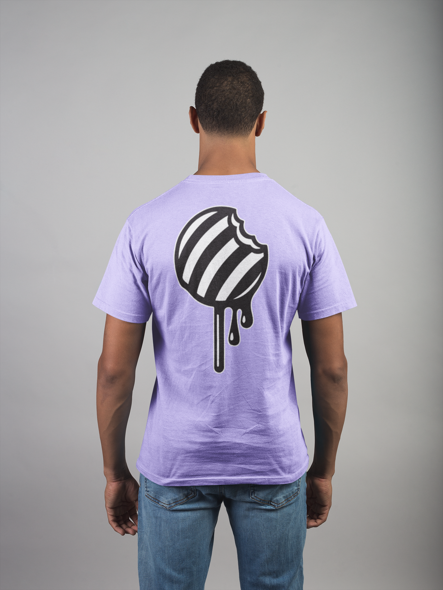 Man wearing a light purple t-shirt with a black and white striped round candy on stick graphic design on the back against a gray background